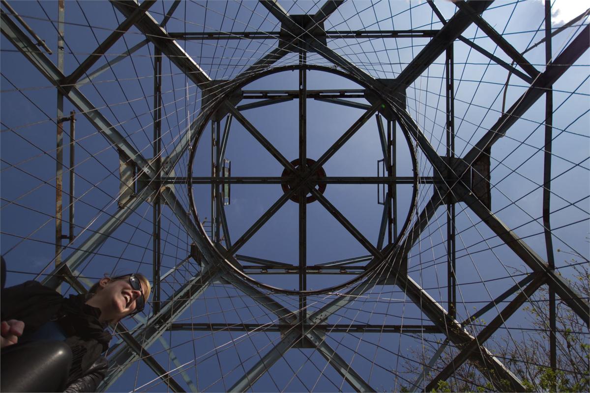 Van onderaf gefotografeerde stalen kraanconstructie; in de vierkante opening is een ronde ring met een geweven net van touw gespannen.
