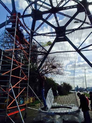 Construction photograph inside the crane base: an orange mobile scaffold, two people at work and the net being pulled up from the ground.