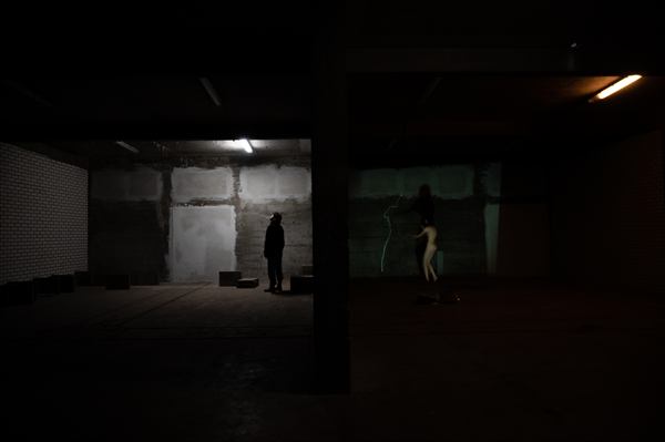 Donkere betonnen ruimte in een munitiebunker met een verlichte projectie op de achterwand en een figuur die stilstaat in het licht.