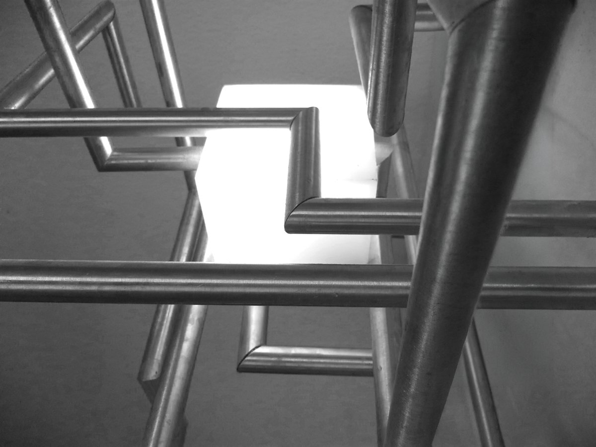 Detail of the lamp: aluminium tubes turning at right angles, with the white light of the opal perspex box behind them.