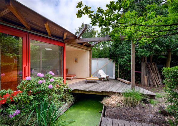 The Brughuis at the end of the garden: a timber work house with red frames and a large sliding door, with a wooden deck bridging a ditch to the terrace.