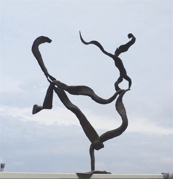 Donkere gesmede stalen sculptuur tegen een bewolkte lucht, balancerend op één punt.